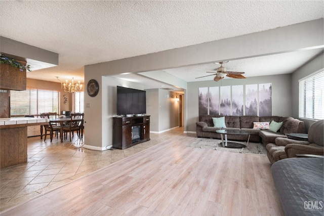 living area with light wood-type flooring, baseboards, a textured ceiling, and ceiling fan with notable chandelier