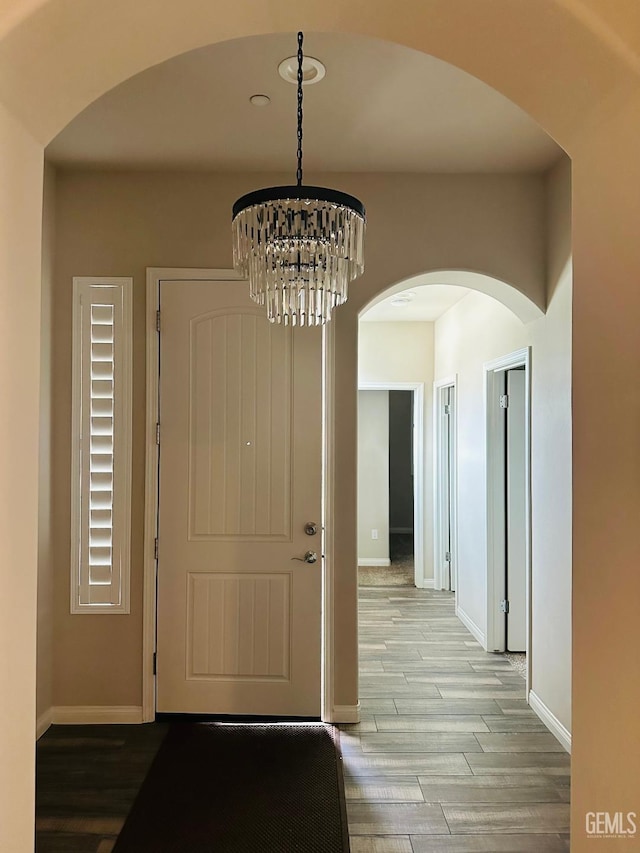 entrance foyer featuring wood finished floors, a notable chandelier, and baseboards