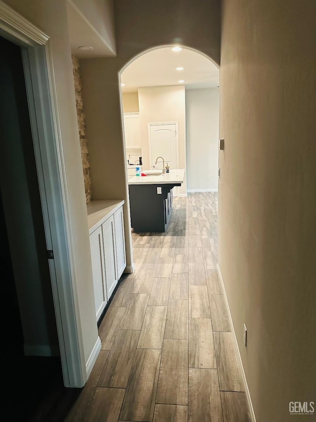 corridor featuring a sink, recessed lighting, light wood-style flooring, and arched walkways