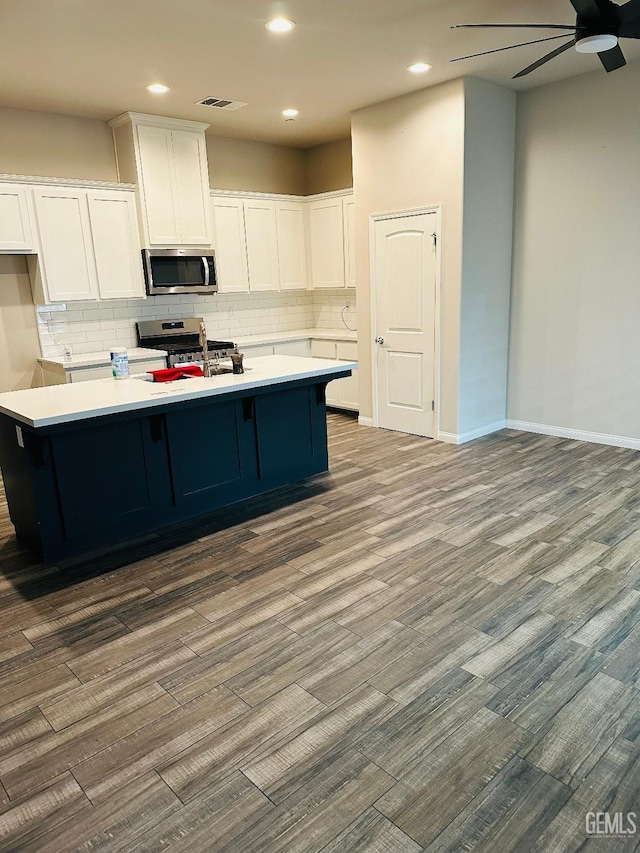 kitchen with dark wood-style flooring, stainless steel appliances, a ceiling fan, backsplash, and white cabinetry