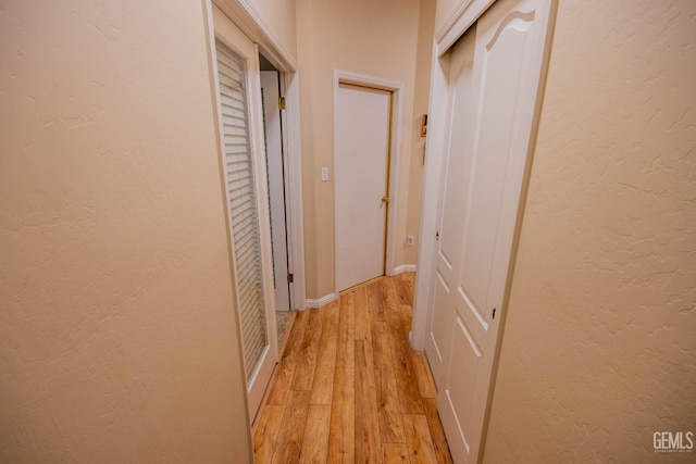 corridor featuring light wood-style floors, baseboards, and a textured wall