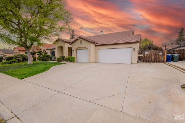 mediterranean / spanish home with stucco siding, a lawn, driveway, an attached garage, and a tiled roof