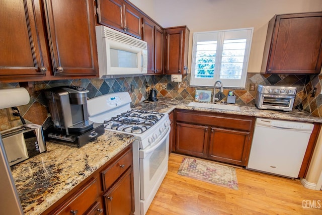 kitchen featuring white appliances, light stone countertops, a sink, light wood-style floors, and backsplash