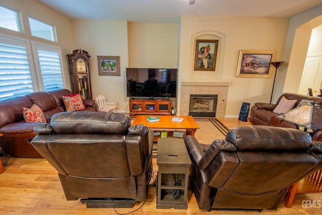 living room with a fireplace, light wood-style floors, arched walkways, and baseboards