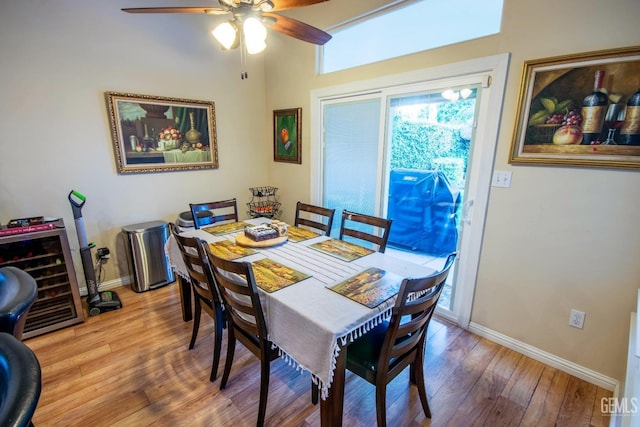 dining room with wood finished floors, wine cooler, a ceiling fan, and baseboards