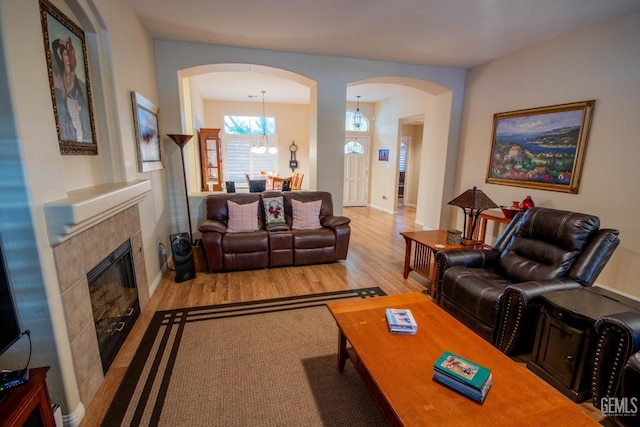 living area with arched walkways, a notable chandelier, a tile fireplace, and light wood finished floors