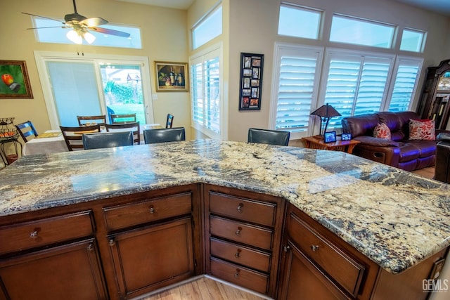 kitchen with light wood-style flooring, light stone counters, brown cabinetry, and ceiling fan