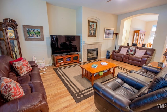 living room featuring a tiled fireplace, light wood-style floors, arched walkways, and baseboards