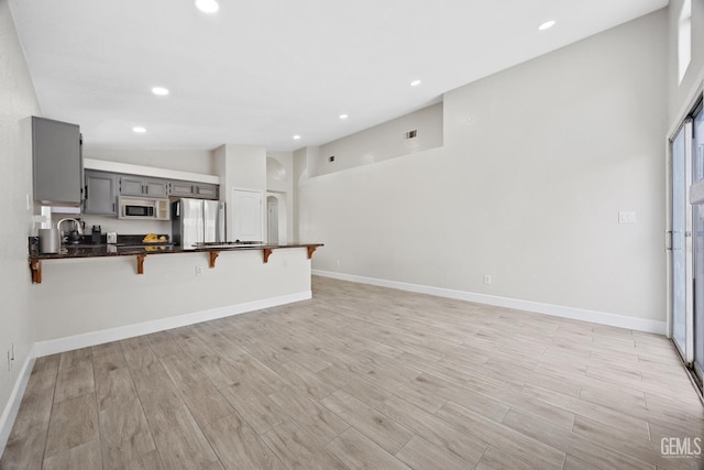 kitchen featuring a breakfast bar area, gray cabinetry, vaulted ceiling, stainless steel fridge, and kitchen peninsula