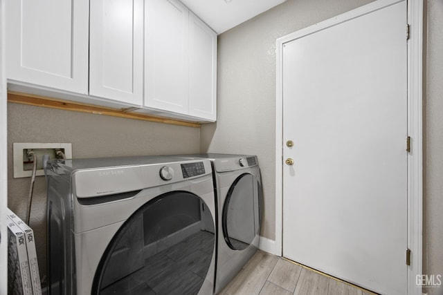 clothes washing area with cabinets, light hardwood / wood-style floors, and washing machine and clothes dryer