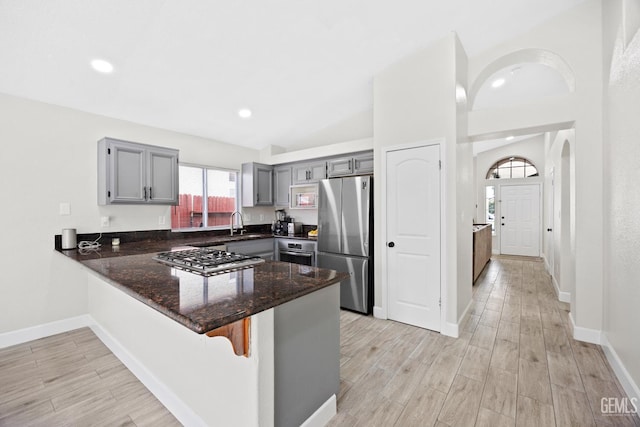 kitchen with light wood-type flooring, dark stone counters, gray cabinets, kitchen peninsula, and stainless steel appliances