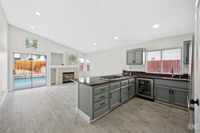 kitchen with wine cooler, sink, vaulted ceiling, kitchen peninsula, and a tile fireplace