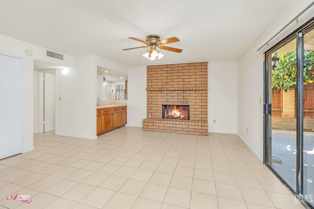 unfurnished living room featuring ceiling fan, a brick fireplace, light tile patterned flooring, and a textured ceiling