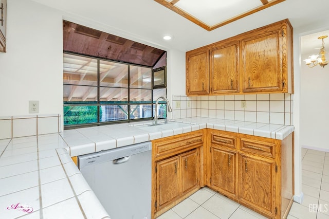 kitchen with tasteful backsplash, dishwasher, tile countertops, sink, and a chandelier