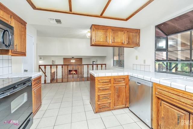 kitchen featuring tile counters, kitchen peninsula, range with electric stovetop, a brick fireplace, and stainless steel dishwasher