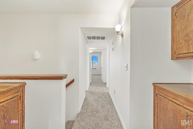 hallway with light carpet and a textured ceiling