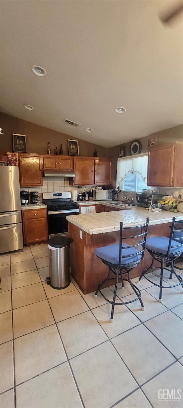 kitchen featuring tasteful backsplash, tile countertops, vaulted ceiling, and appliances with stainless steel finishes