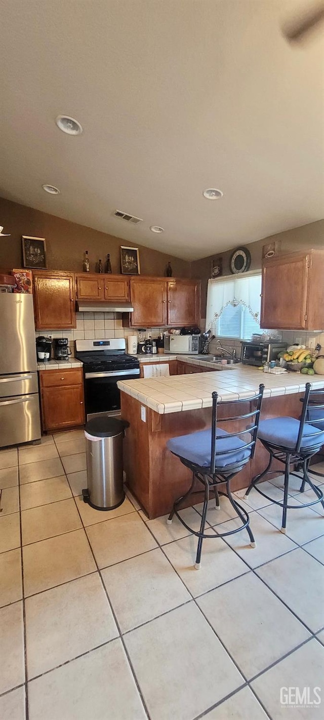 kitchen featuring lofted ceiling, light tile patterned floors, appliances with stainless steel finishes, tasteful backsplash, and tile counters