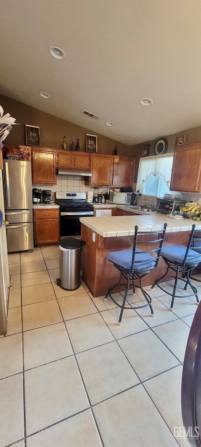 kitchen featuring tile counters, tasteful backsplash, lofted ceiling, light tile patterned flooring, and appliances with stainless steel finishes