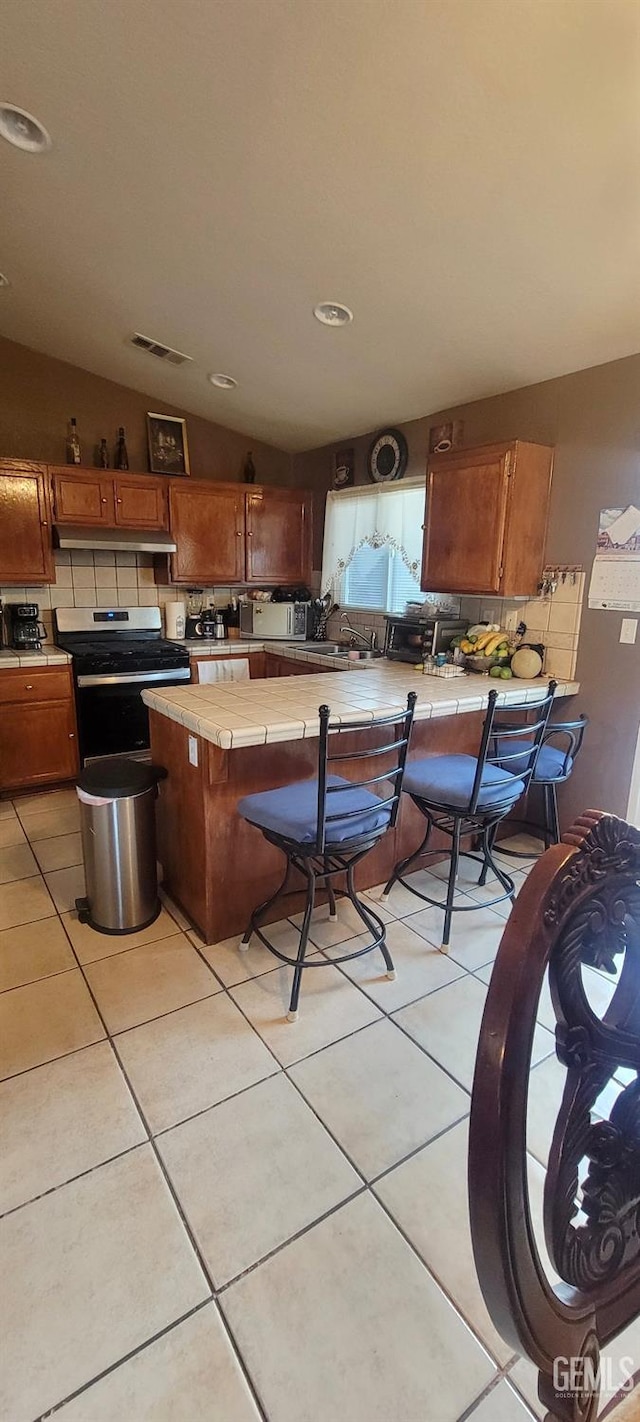 kitchen with decorative backsplash, vaulted ceiling, light tile patterned floors, electric range, and tile counters