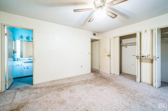 unfurnished bedroom featuring multiple closets, ceiling fan, ensuite bathroom, and light colored carpet