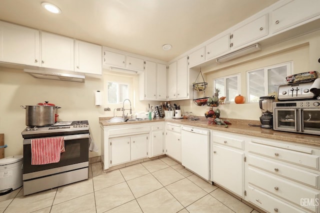 kitchen with white dishwasher, white cabinets, sink, light tile patterned floors, and stainless steel range