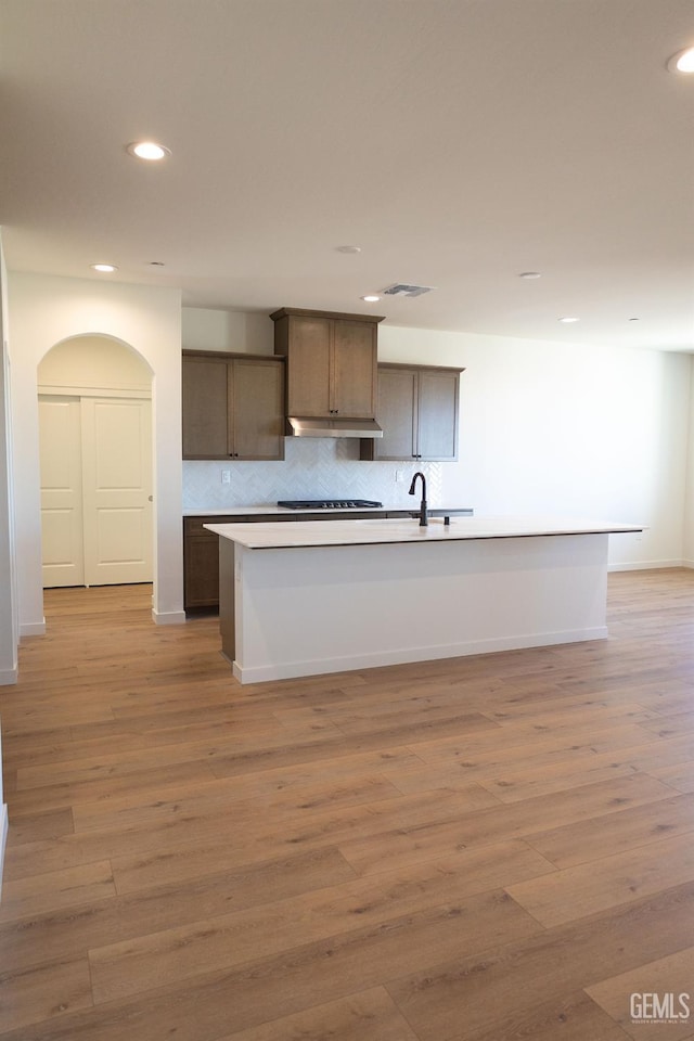 12706 Kinnick Ct, Bakersfield, CA 93311 - kitchen featuring under cabinet range hood, recessed lighting, a kitchen island with sink, decorative backsplash, and light wood finished floors