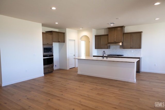 12706 Kinnick Ct, Bakersfield, CA 93311 - kitchen with arched walkways, under cabinet range hood, recessed lighting, tasteful backsplash, and light wood-style flooring