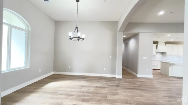 unfurnished dining area featuring a chandelier, arched walkways, recessed lighting, baseboards, and light wood-style floors