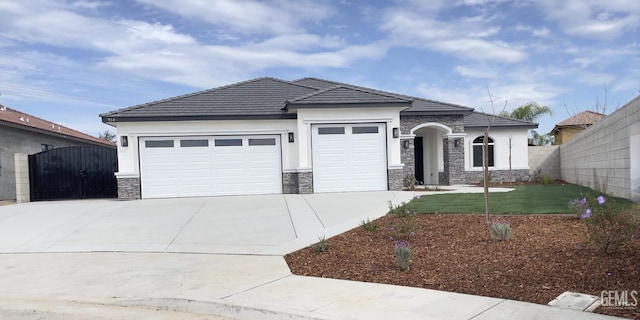 view of front of home with driveway, stone siding, an attached garage, and a gate