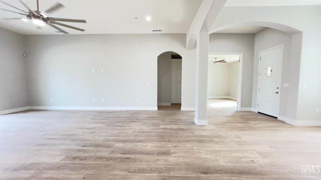 unfurnished room with ceiling fan, arched walkways, light wood-style flooring, visible vents, and baseboards