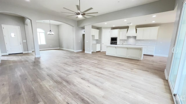 kitchen with open floor plan, stainless steel microwave, custom exhaust hood, and ceiling fan with notable chandelier