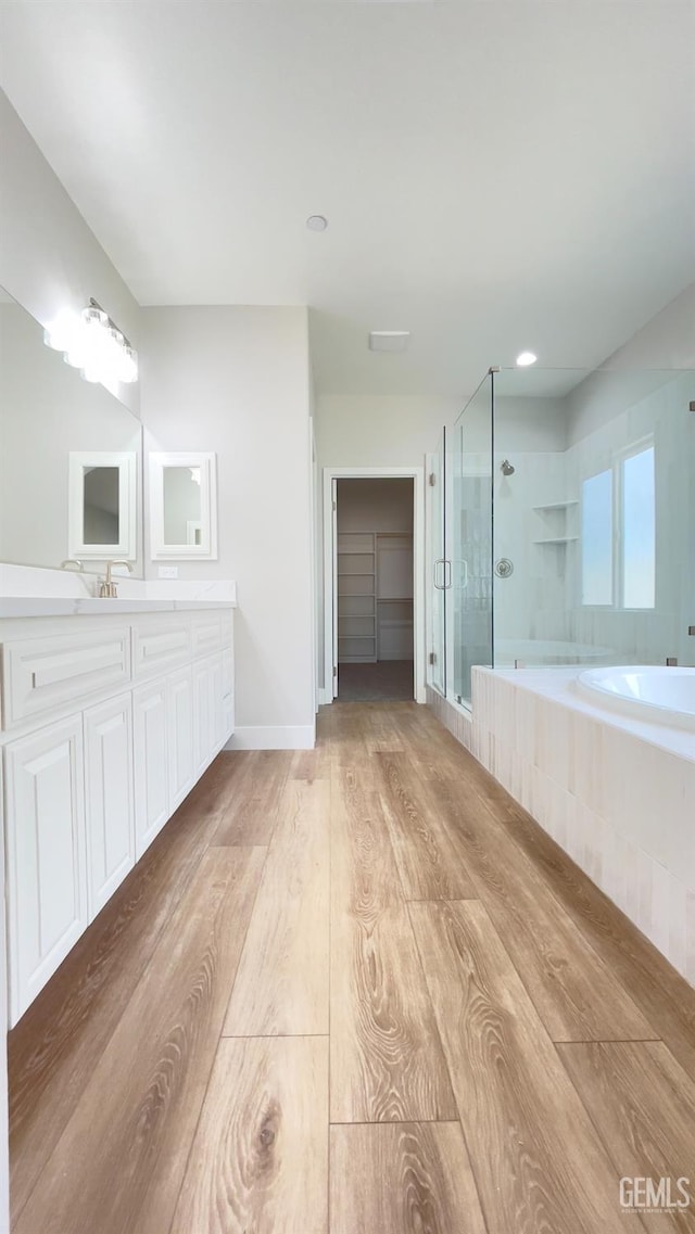 bathroom featuring a garden tub, wood finished floors, vanity, baseboards, and a shower stall