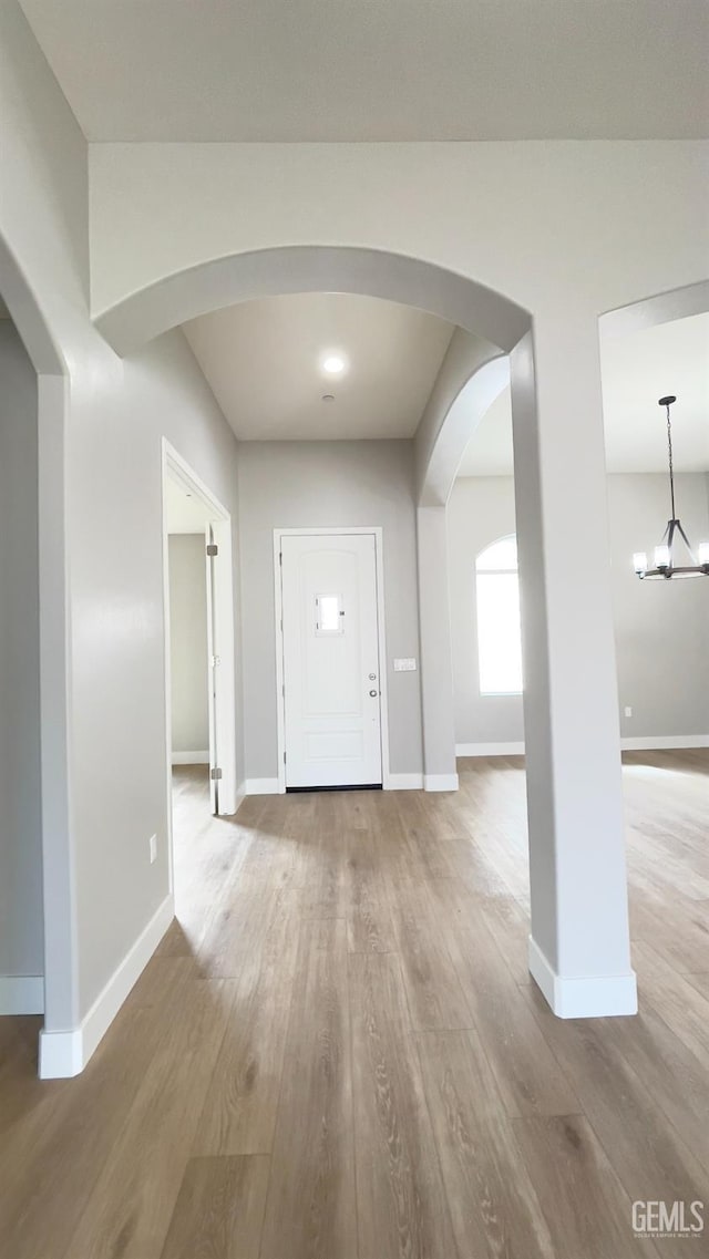 foyer with arched walkways, a notable chandelier, baseboards, and wood finished floors