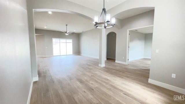 interior space featuring arched walkways, light wood finished floors, ceiling fan with notable chandelier, and baseboards