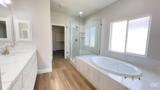 bathroom with a spacious closet, a stall shower, vanity, wood finished floors, and a bath