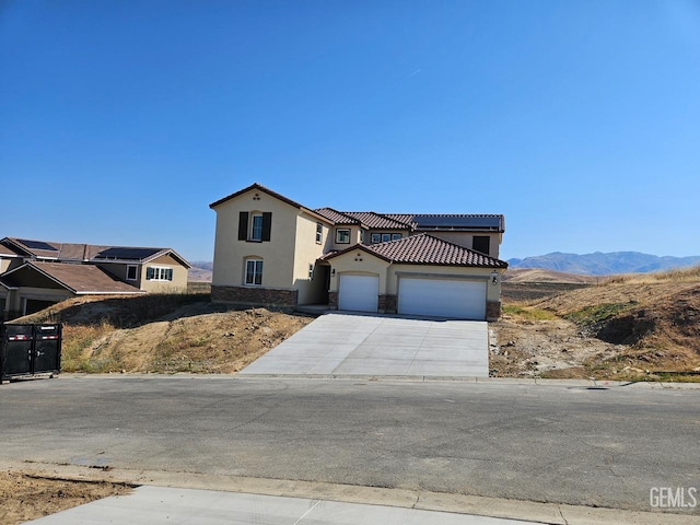 mediterranean / spanish house featuring a garage, stone siding, stucco siding, a tiled roof, and driveway