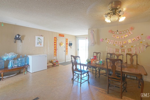 dining room featuring a textured ceiling, ceiling fan, and wood walls