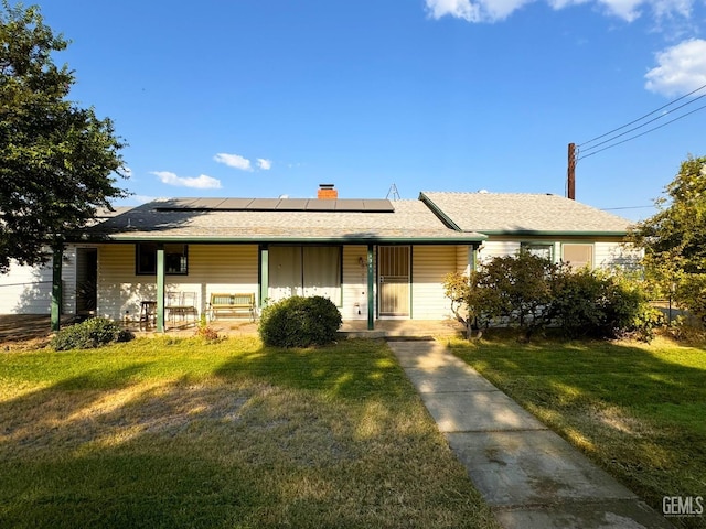 ranch-style house with a front lawn, roof mounted solar panels, covered porch, and a chimney