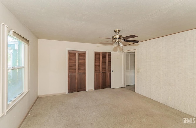 unfurnished bedroom with a ceiling fan, multiple closets, and light carpet
