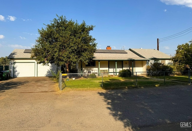 ranch-style home featuring a fenced front yard, a chimney, solar panels, dirt driveway, and a garage