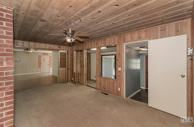 carpeted spare room with visible vents, ceiling fan, wooden walls, and wooden ceiling
