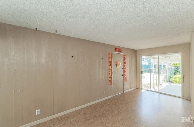 spare room featuring wooden walls, a textured ceiling, and baseboards