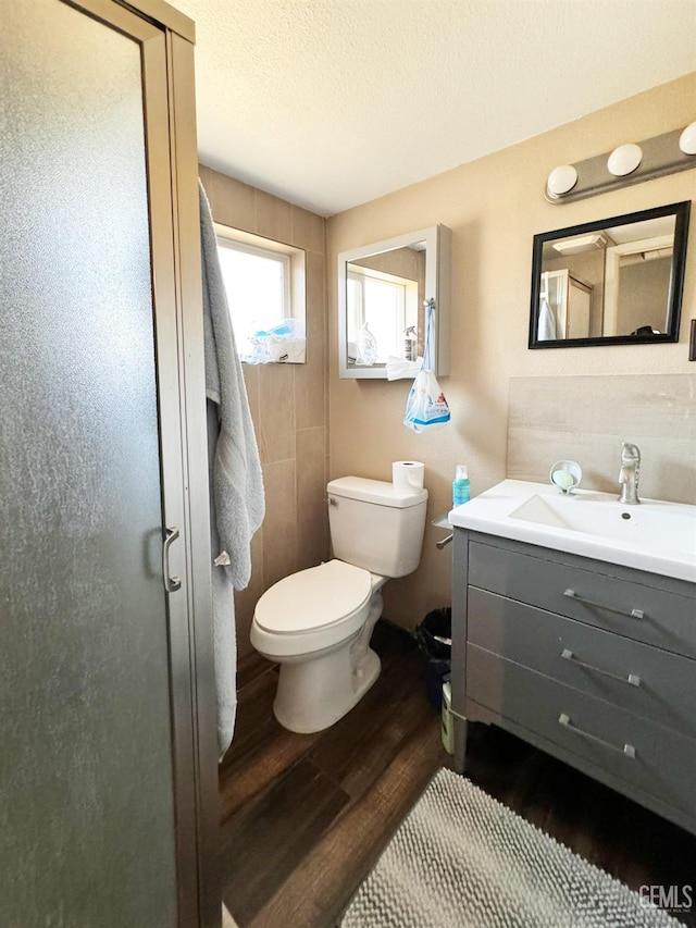 bathroom featuring wood-type flooring, a textured ceiling, toilet, a shower with door, and vanity