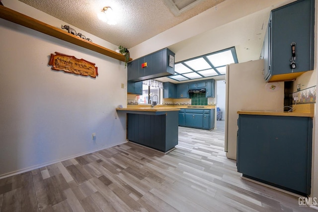 4508 Glengary Pl, Bakersfield, CA 93313 - kitchen with blue cabinets, a peninsula, light wood-type flooring, a textured ceiling, and under cabinet range hood