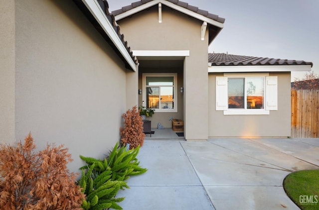 entrance to property with a tile roof, fence, and stucco siding