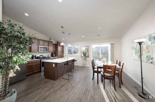 kitchen with a center island with sink, appliances with stainless steel finishes, a breakfast bar, dark wood-style flooring, and vaulted ceiling