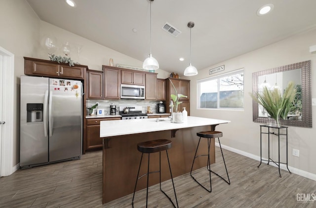 kitchen featuring visible vents, lofted ceiling, an island with sink, stainless steel appliances, and light countertops