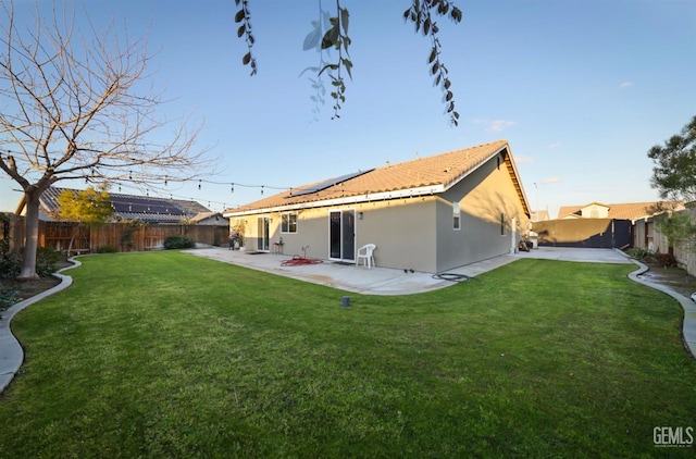 rear view of house with a patio, a yard, solar panels, and a fenced backyard