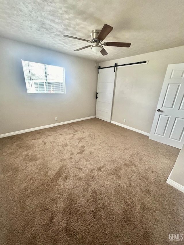 unfurnished bedroom featuring carpet flooring, a textured ceiling, and a barn door